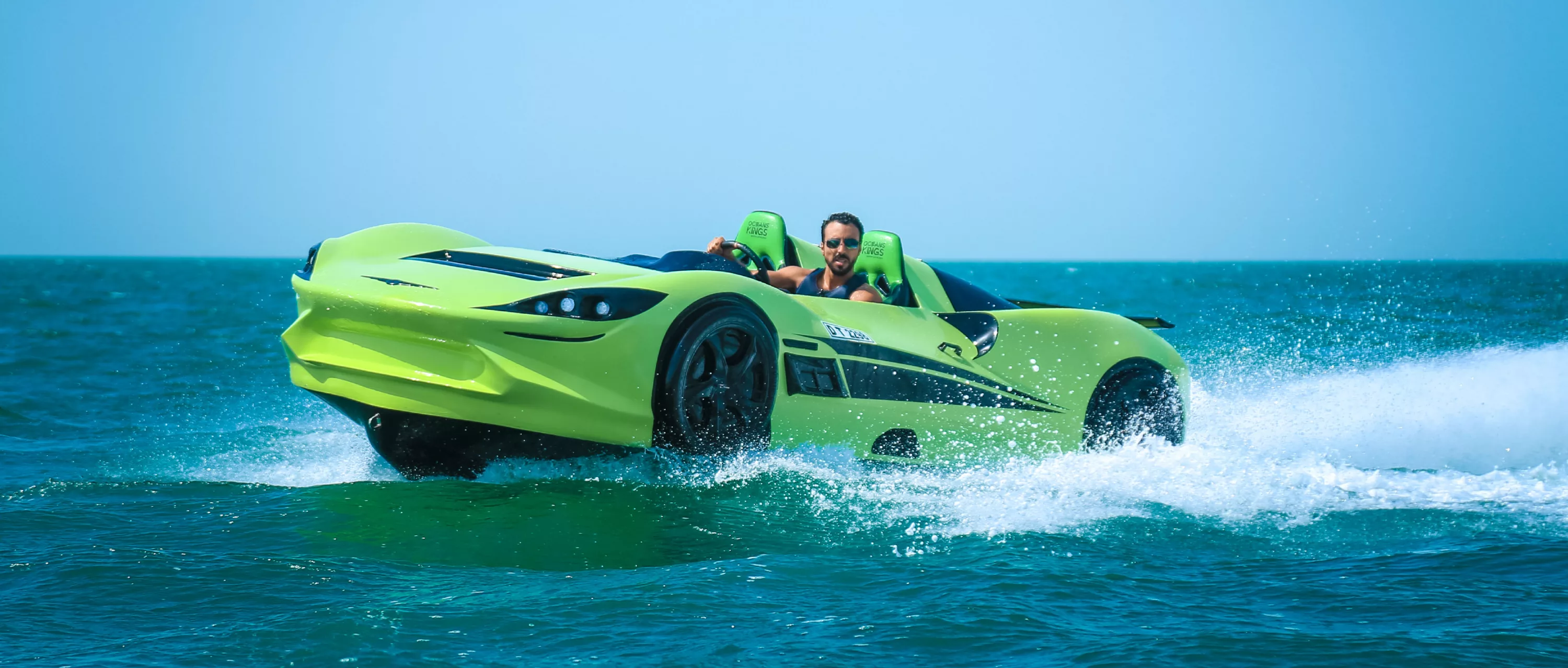 A bright green jet car speeds across the water in Dubai, UAE, during a Hydro Water Sports adventure, creating a dramatic splash under a clear blue sky.